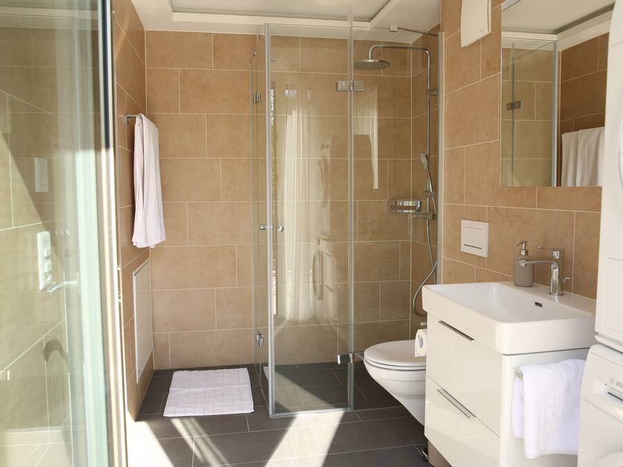 A modern bathroom with a glass-enclosed shower, a white sink, and a Bosch washing machine.