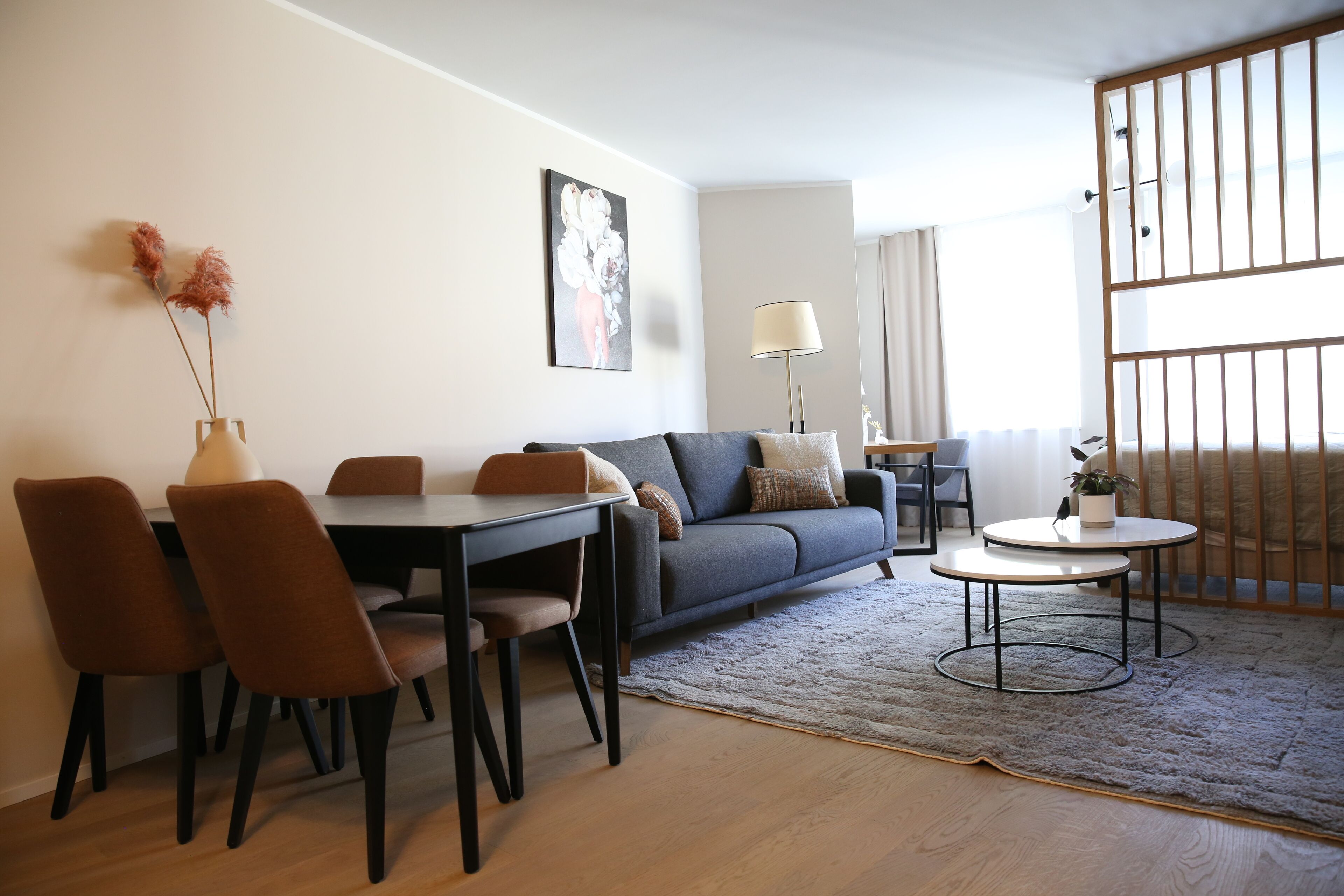 Een moderne woonkamer met een bank, eettafel, stoelen, een lamp en uitzicht door een raam.
