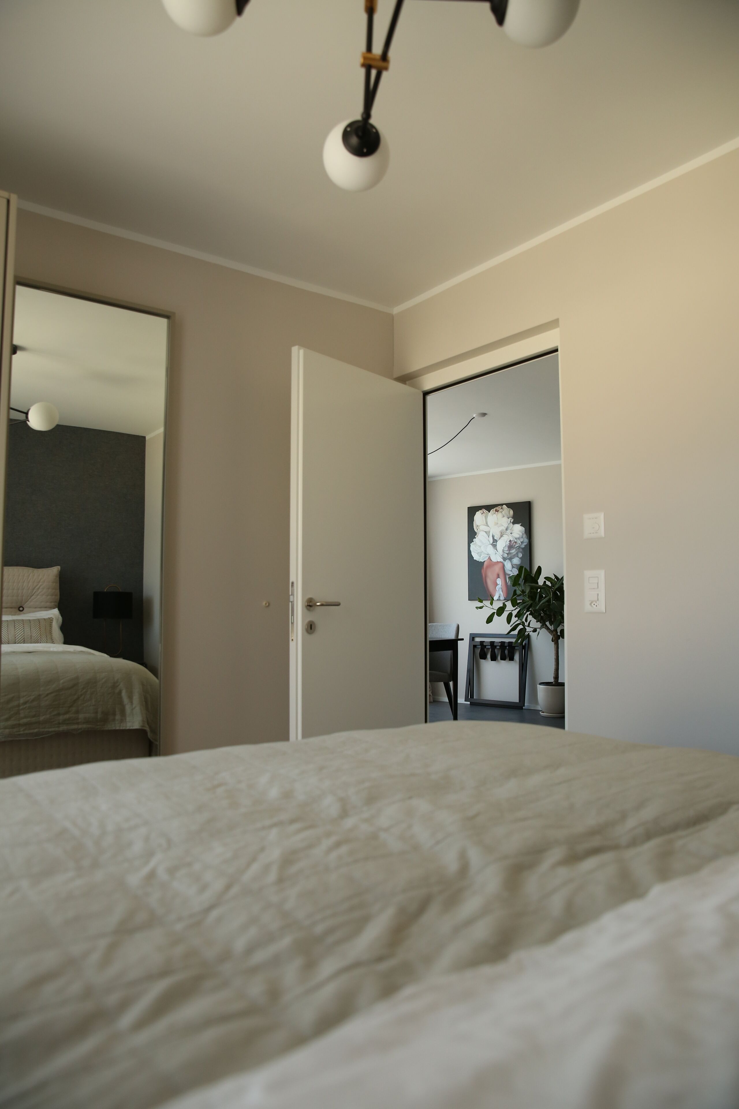 Une chambre à coucher avec un lit, une porte donnant sur une autre pièce, un miroir et un luminaire fixé au mur.