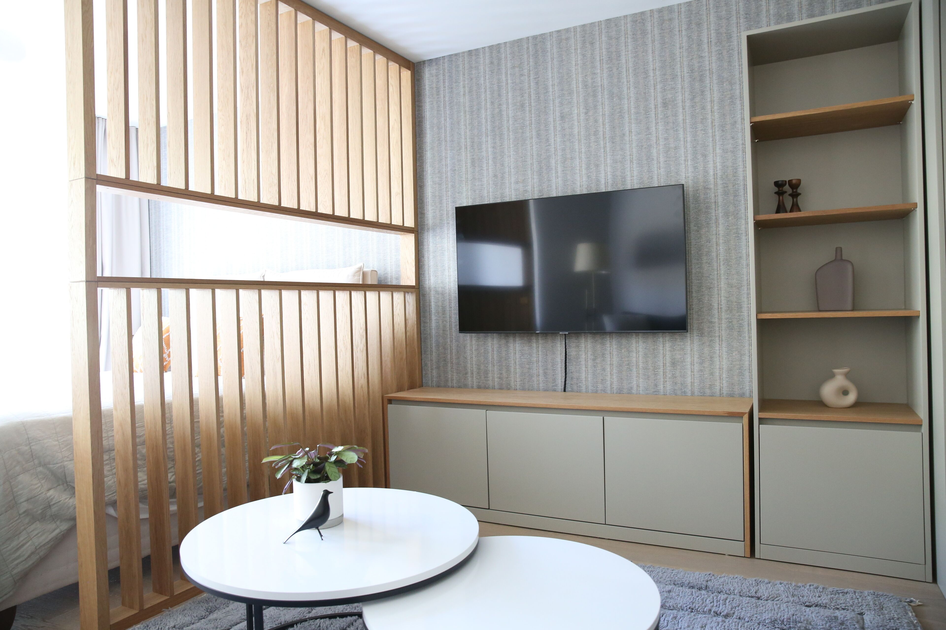 Una sala de estar moderna con un televisor de pantalla plana montado en la pared, una mesa redonda blanca con una planta y un separador de madera.
