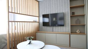 A modern living room with a flat-screen TV mounted on the wall, a round white table with a plant, and a wooden partition.
