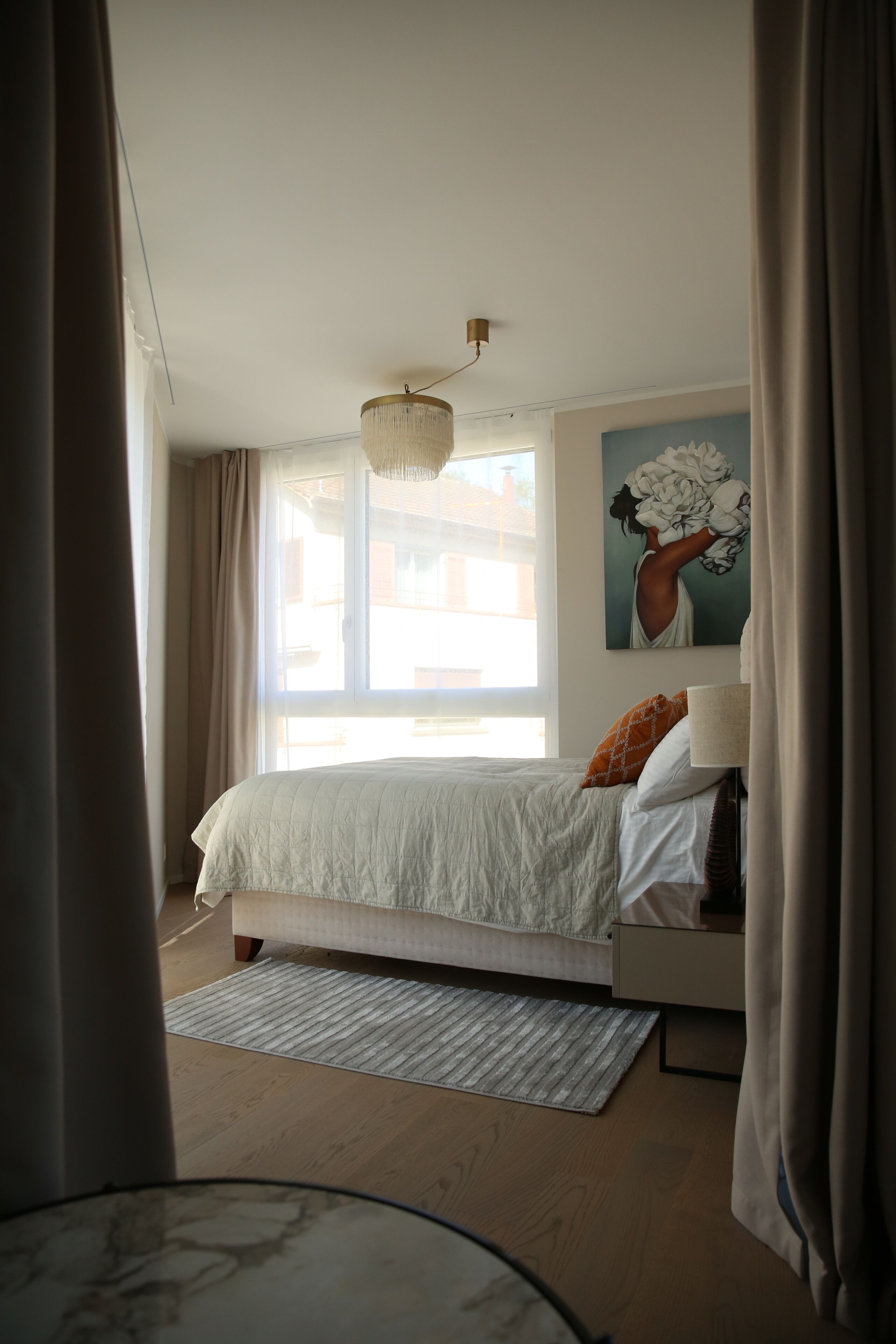 Een slaapkamer met een bed, een raam, een schilderij en een lamp.