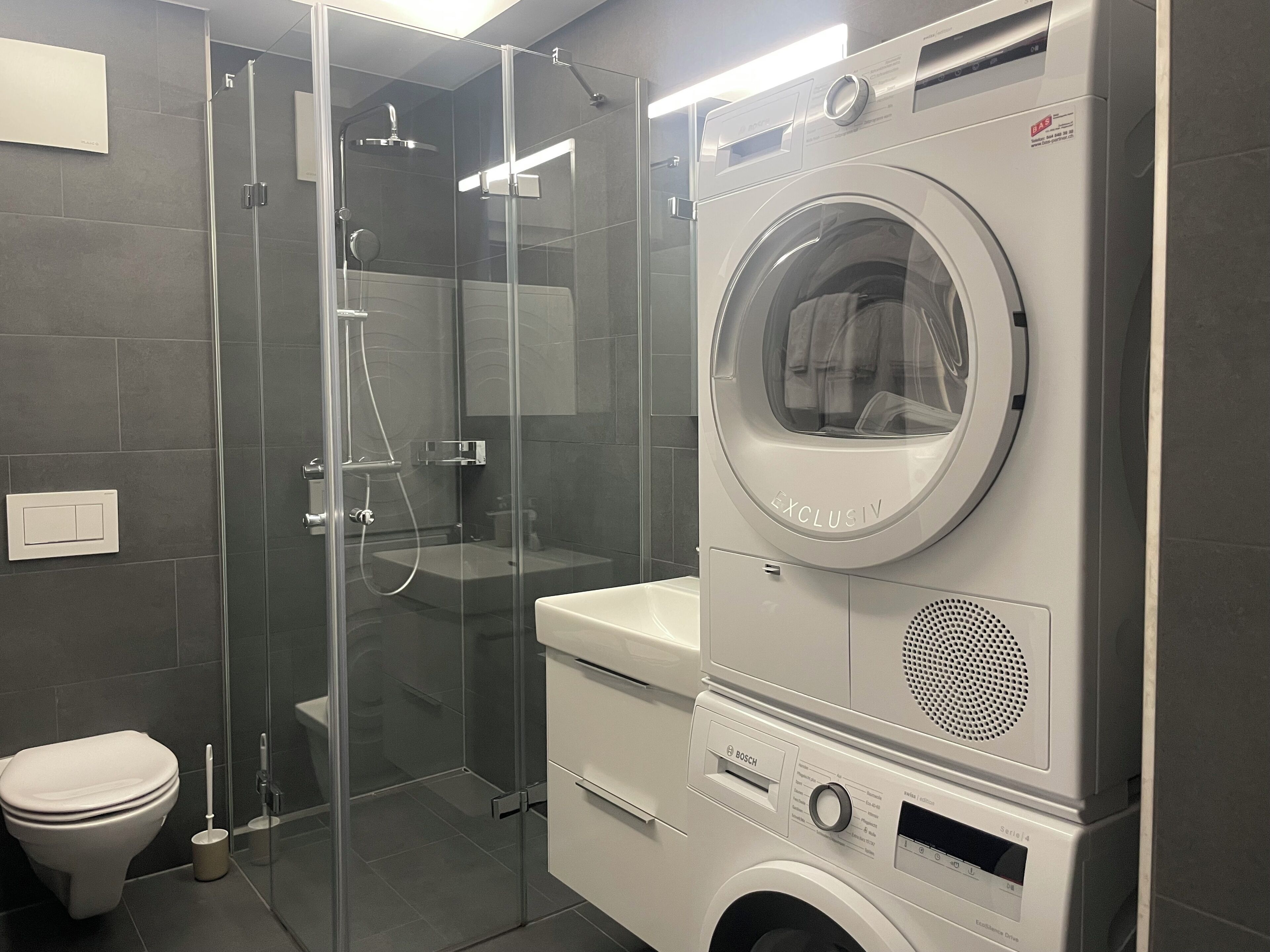 Une salle de bain compacte dotée d’une douche à parois de verre, d’un lave-linge Bosch et de toilettes.