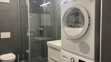 A compact bathroom with a glass-enclosed shower, a Bosch washing machine, and a toilet.