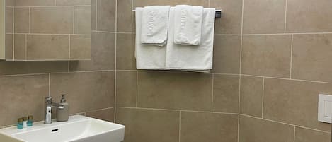 A modern bathroom with a white vanity, a mirror, a towel rack with two towels, and a toilet.