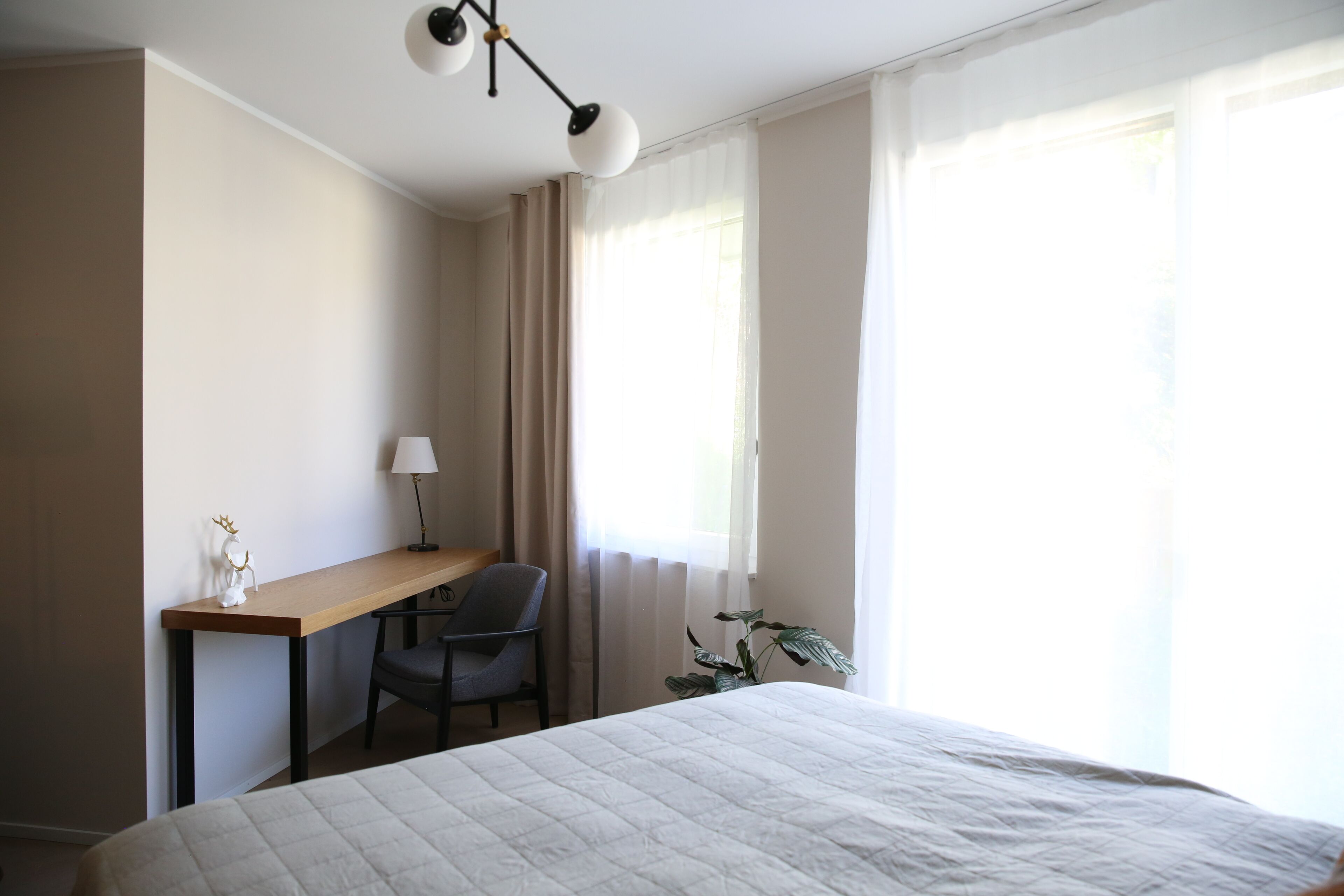 Ein Hotelzimmer mit Bett, Schreibtisch, Stuhl, Lampe und einer Pflanze.