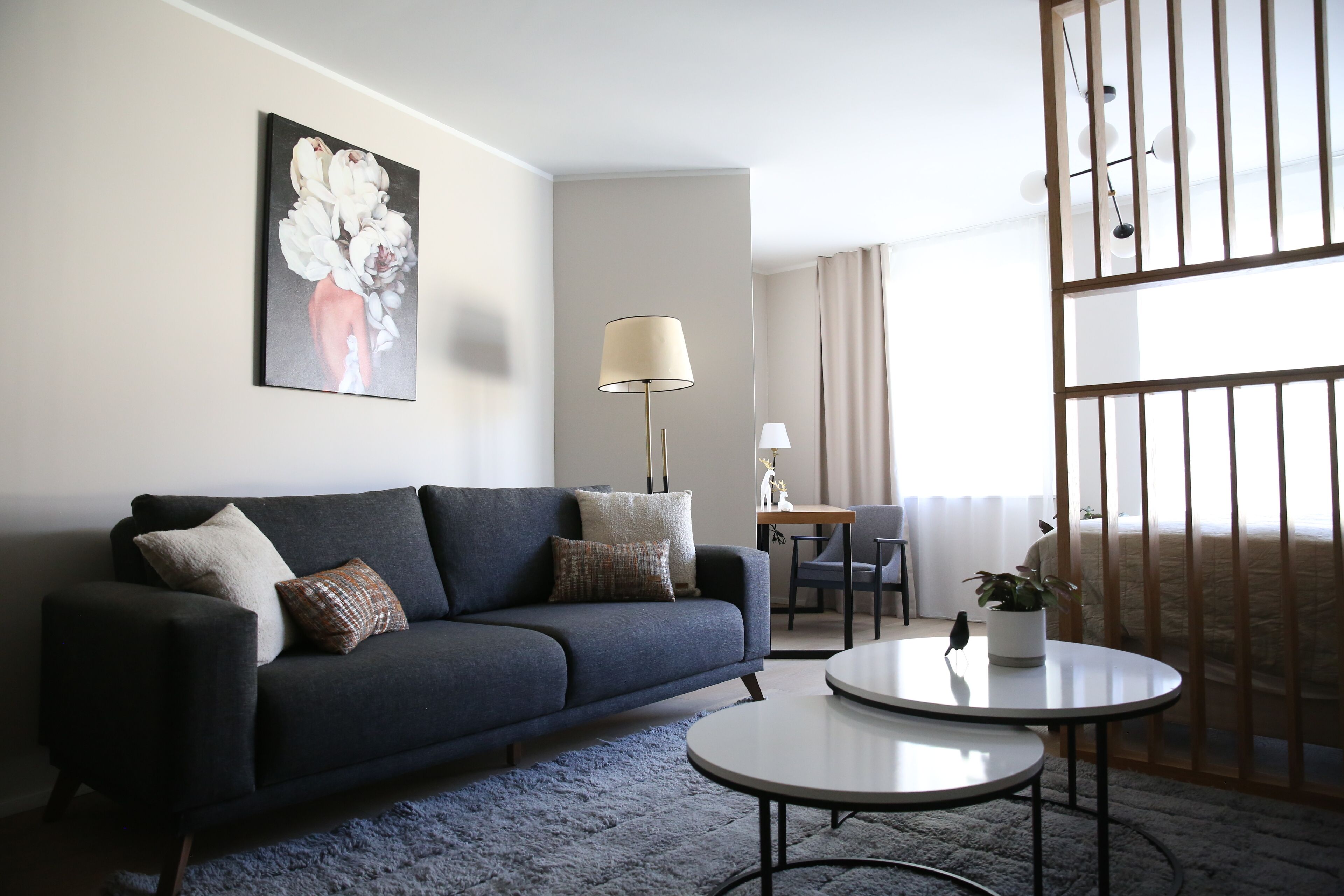 Una sala moderna con un sofá azul oscuro, una mesa de centro redonda y un cuadro de flores en la pared.