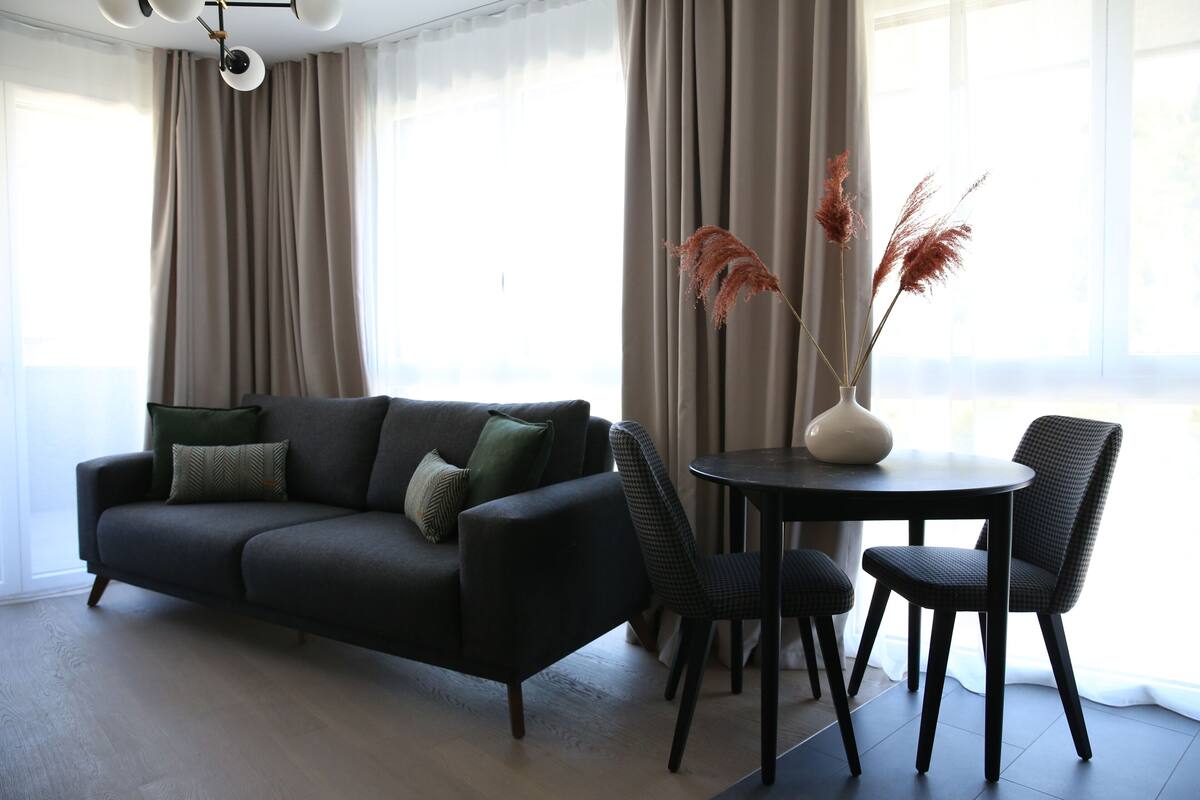 Un salon moderne avec un canapé gris foncé, deux fauteuils assortis, une table ronde et un vase contenant des plantes séchées.