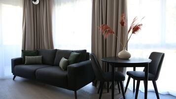 A modern living room with a dark grey sofa, two matching armchairs, a round table, and a vase with dried plants.
