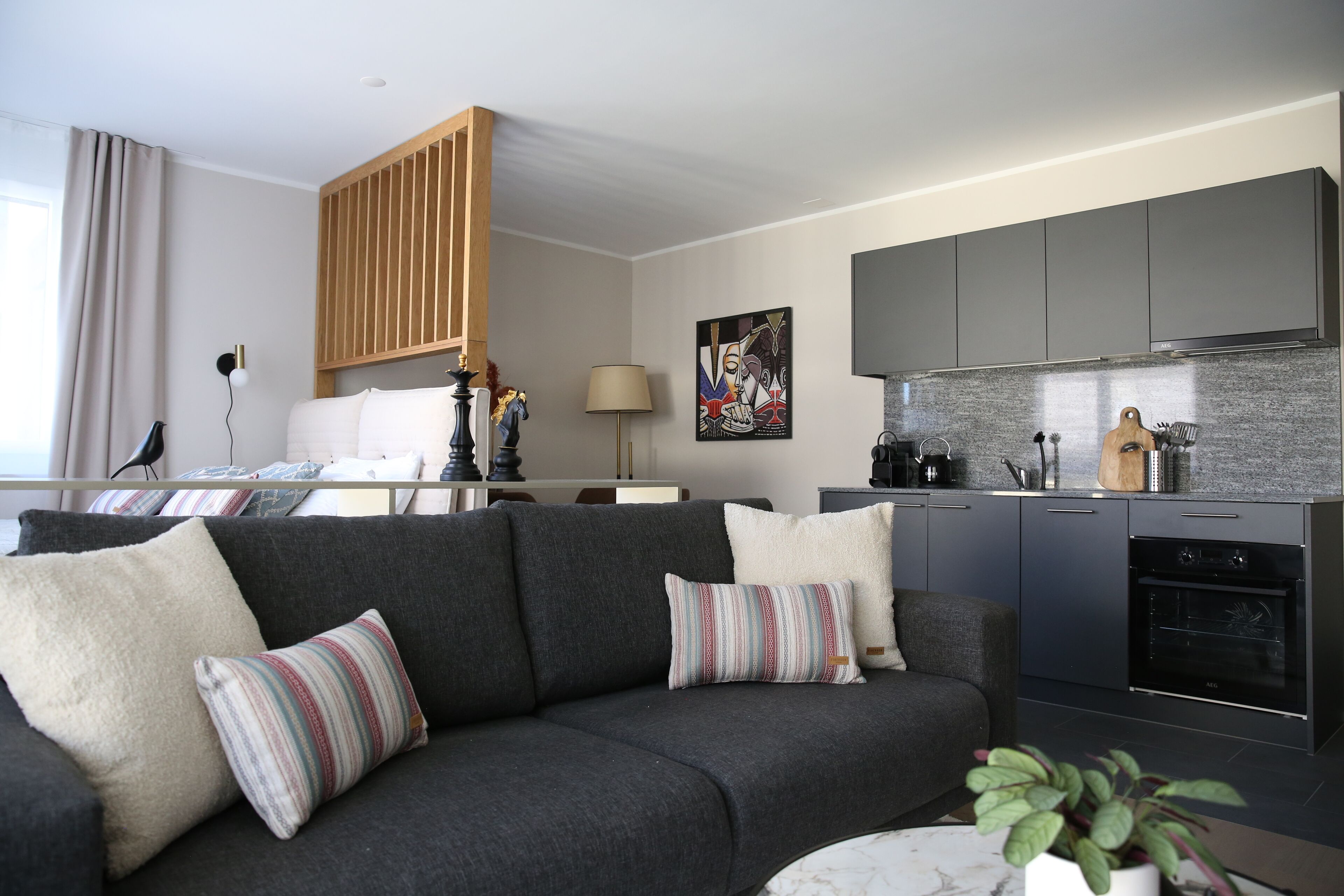 A modern living room with a grey sofa, a small table, and a kitchen area with grey cabinets and a black oven.