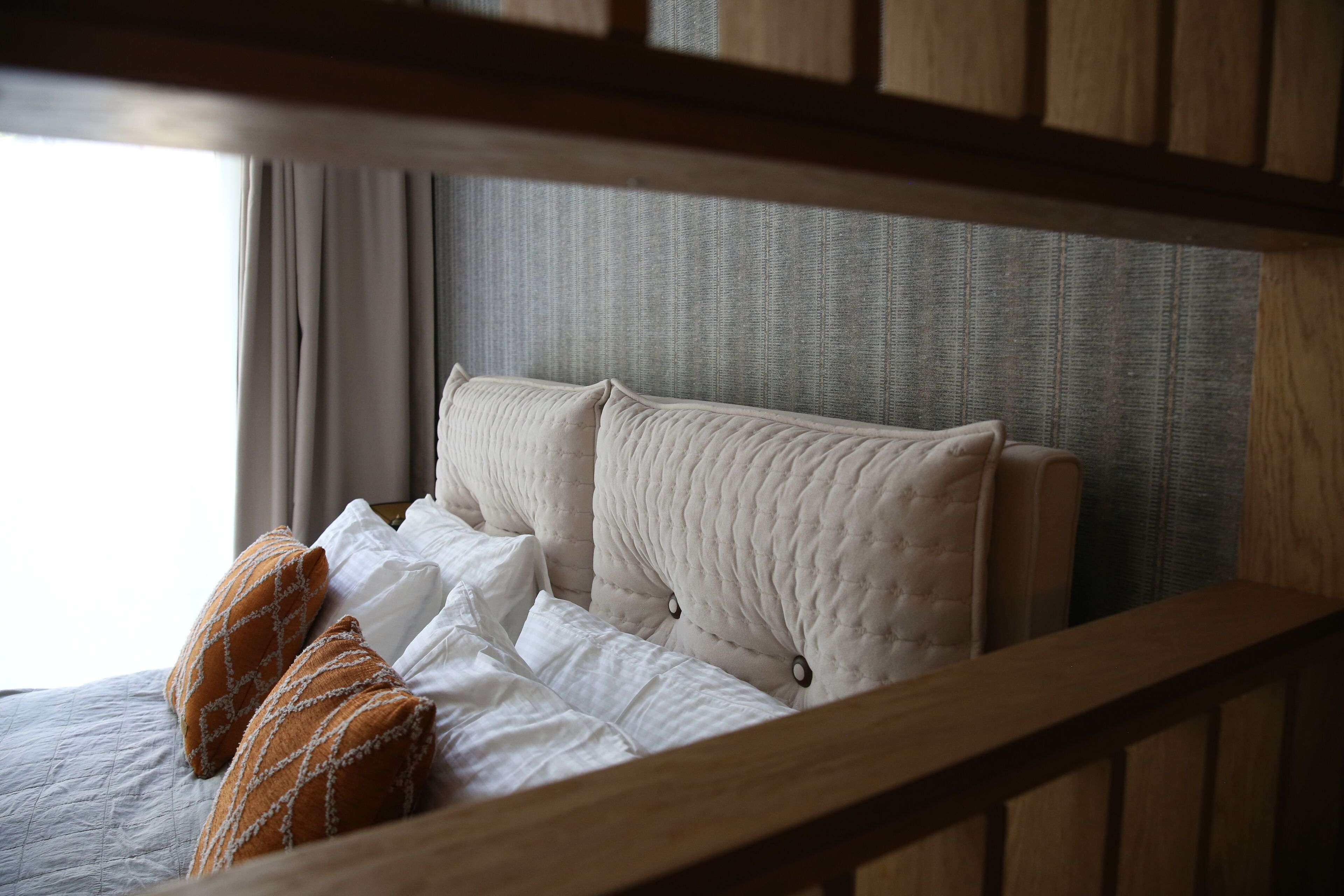 Un lit bien fait, avec des oreillers blancs et orange, une tête de lit matelassée et un cadre de tête de lit en bois.