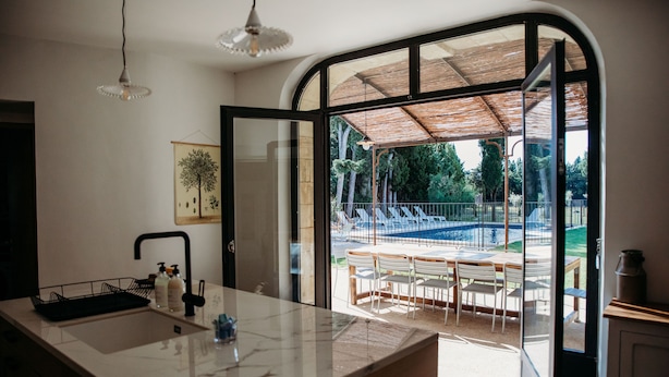 A modern kitchen with a large island, a dining area with outdoor seating, and a view of a swimming pool. - Mas des Ecoliers (Chateaurenard)