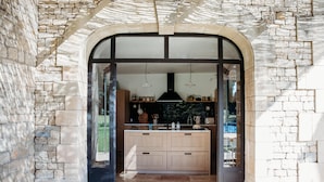 A stone-walled kitchen with a large island, wooden cabinets, and hanging pendant lights. - Mas des Ecoliers (Chateaurenard)