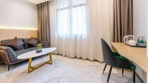 A modern living room with a sofa, a coffee table, a dining area with a chair, and a window with curtains. - Boluo Yanting Business Apartment (Boluo)