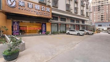 A hotel entrance with a signboard, a parking area, and a street view.