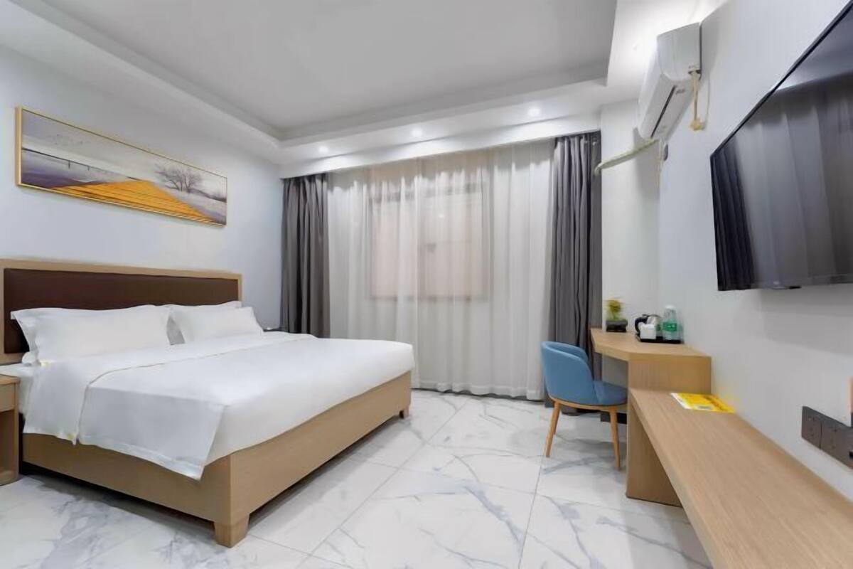 A modern hotel room with a large bed, a desk, a chair, a TV, and a window with curtains.