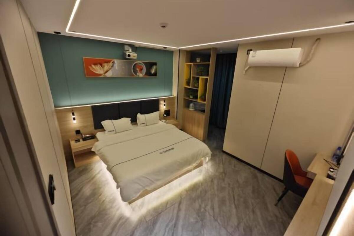 A modern hotel room with a bed, bedside tables, a wardrobe, a desk, and a chair.