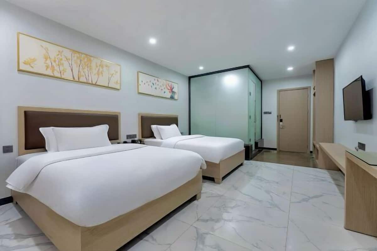 A hotel room with two beds, a TV, a desk, and artwork on the walls.