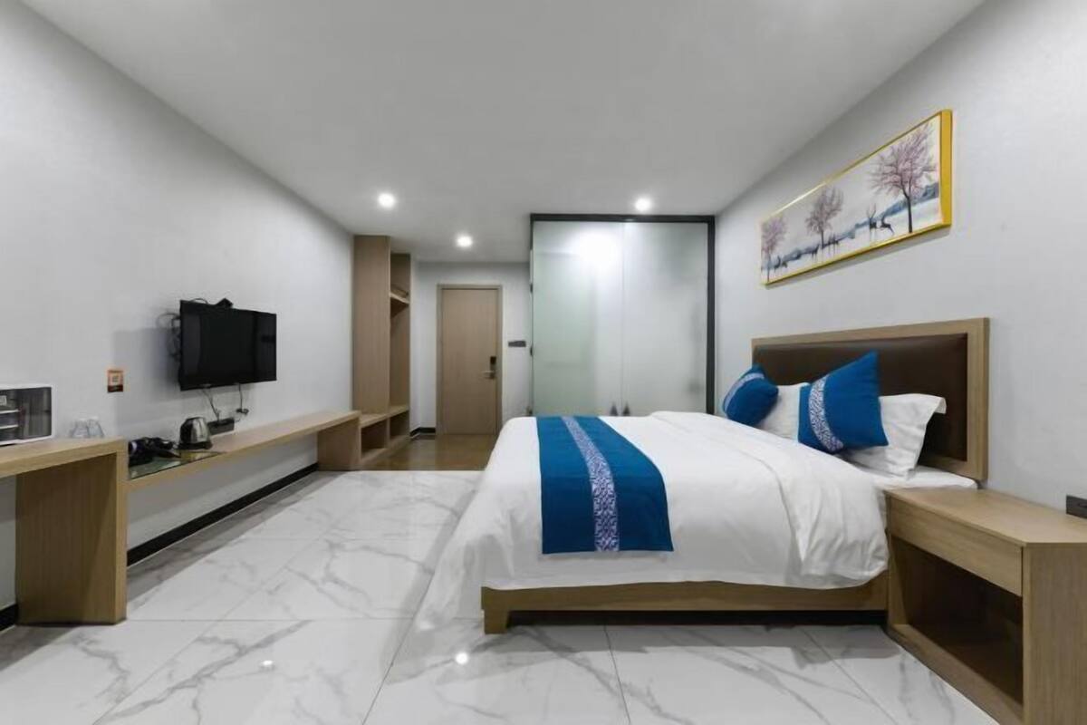 A modern hotel room with a large bed, a television, a desk, and a wardrobe.