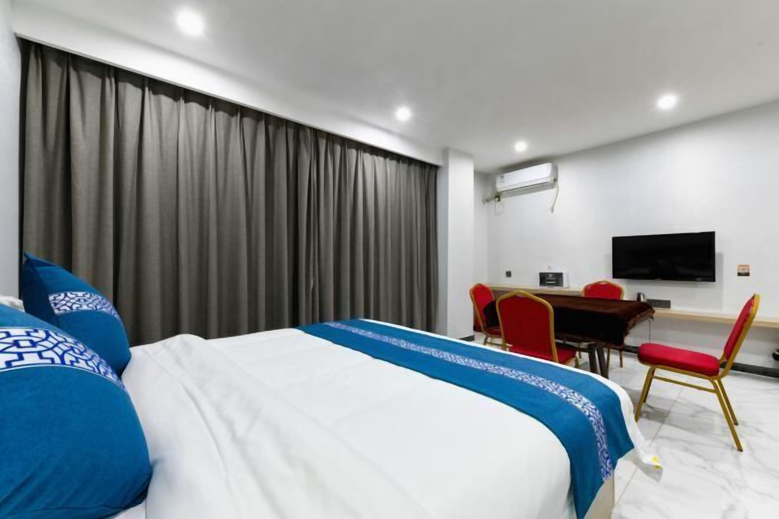 A hotel room with a large bed, a desk with a chair, a flat-screen TV, and a window with curtains.