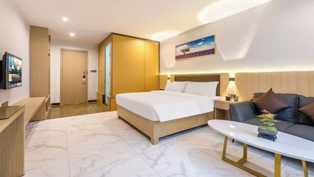 A hotel room with a bed, a sofa, a desk, and a painting on the wall. - Boluo Yanting Business Apartment (Boluo)
