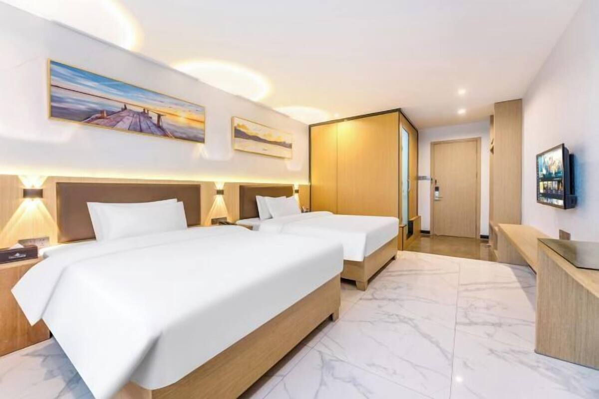 A hotel room with two beds, a desk, a TV, and artwork on the walls.