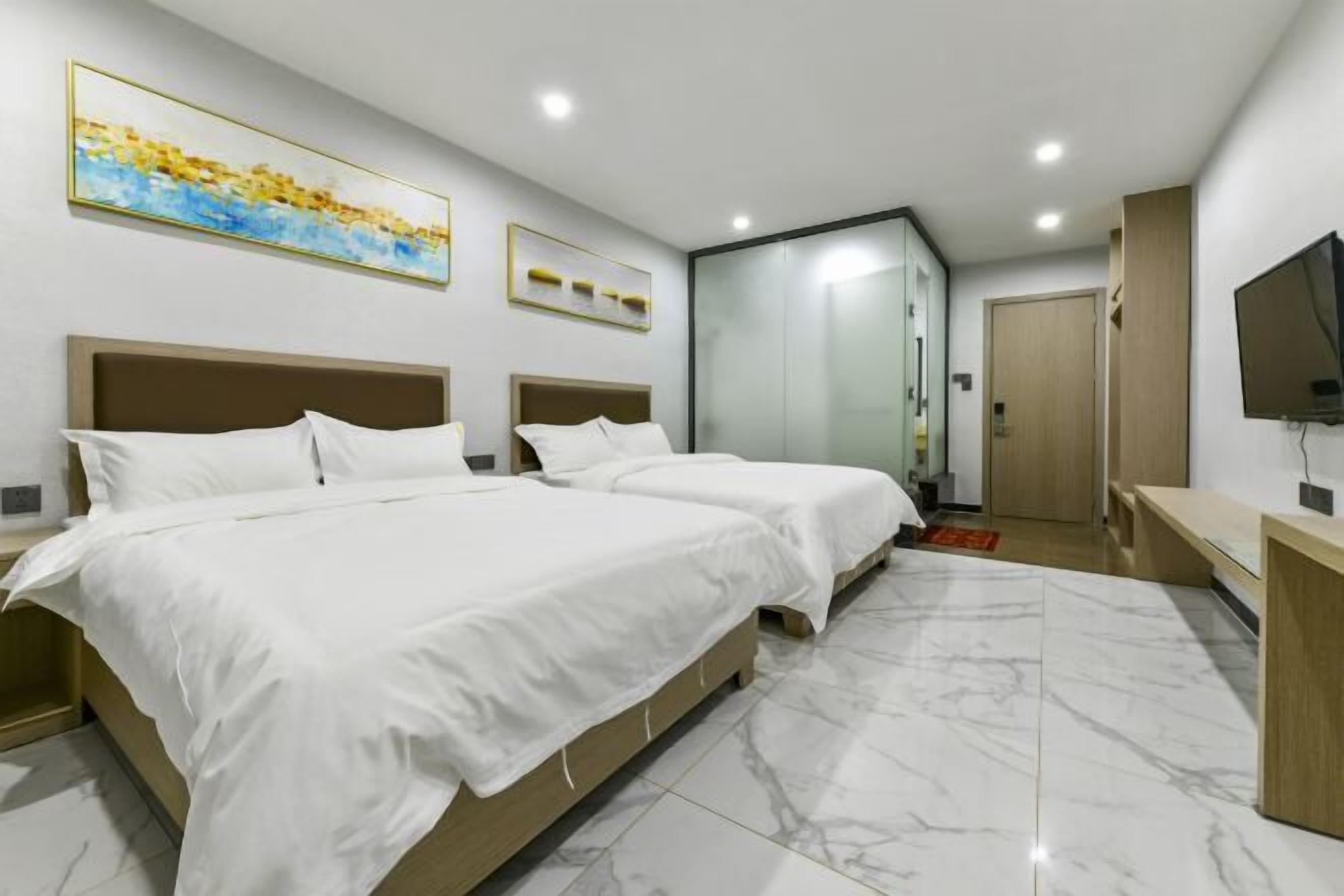 A modern hotel room with two beds, a TV, and a bathroom with a glass door.