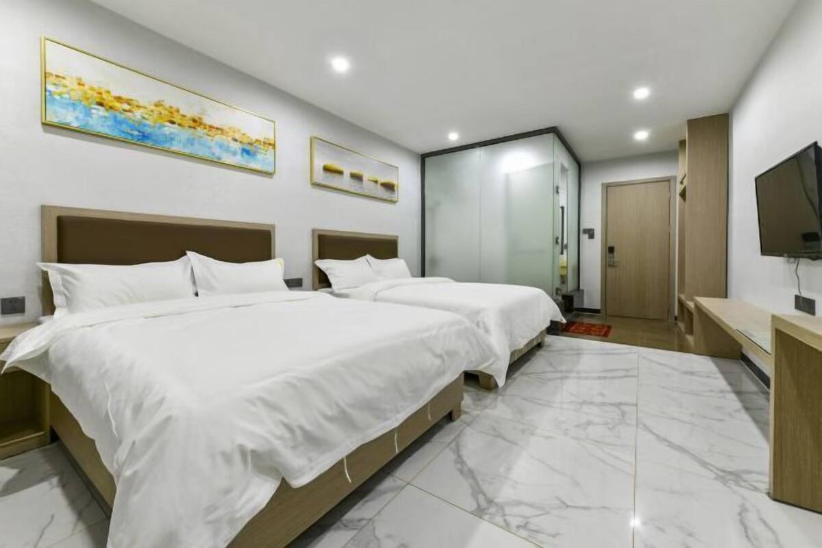 A modern hotel room with two beds, a TV, and a bathroom with a glass door.
