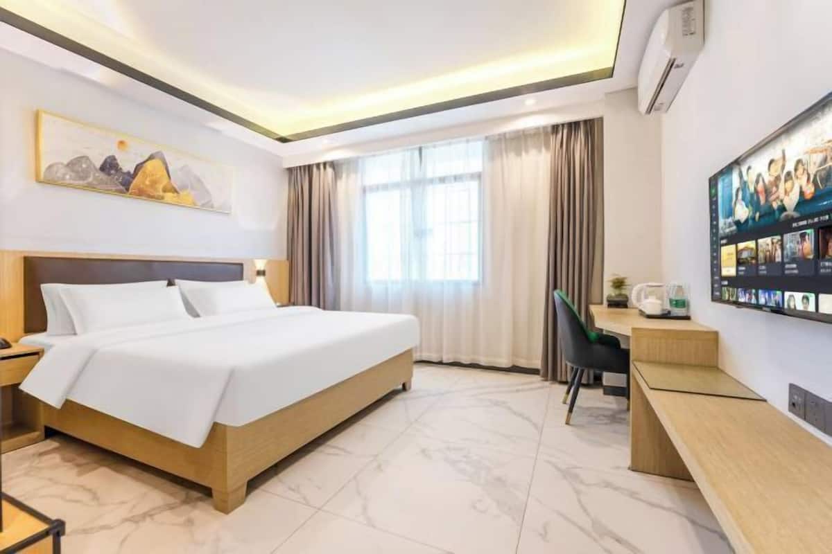 A hotel room with a large bed, a desk, a chair, a flat-screen TV, and a window with curtains.