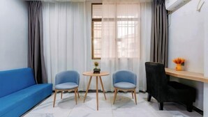 A room with a blue sofa, two blue chairs, a small round table, a black chair, a wooden shelf with a vase, and a window with sheer curtains. - Boluo Yanting Business Apartment (Boluo)