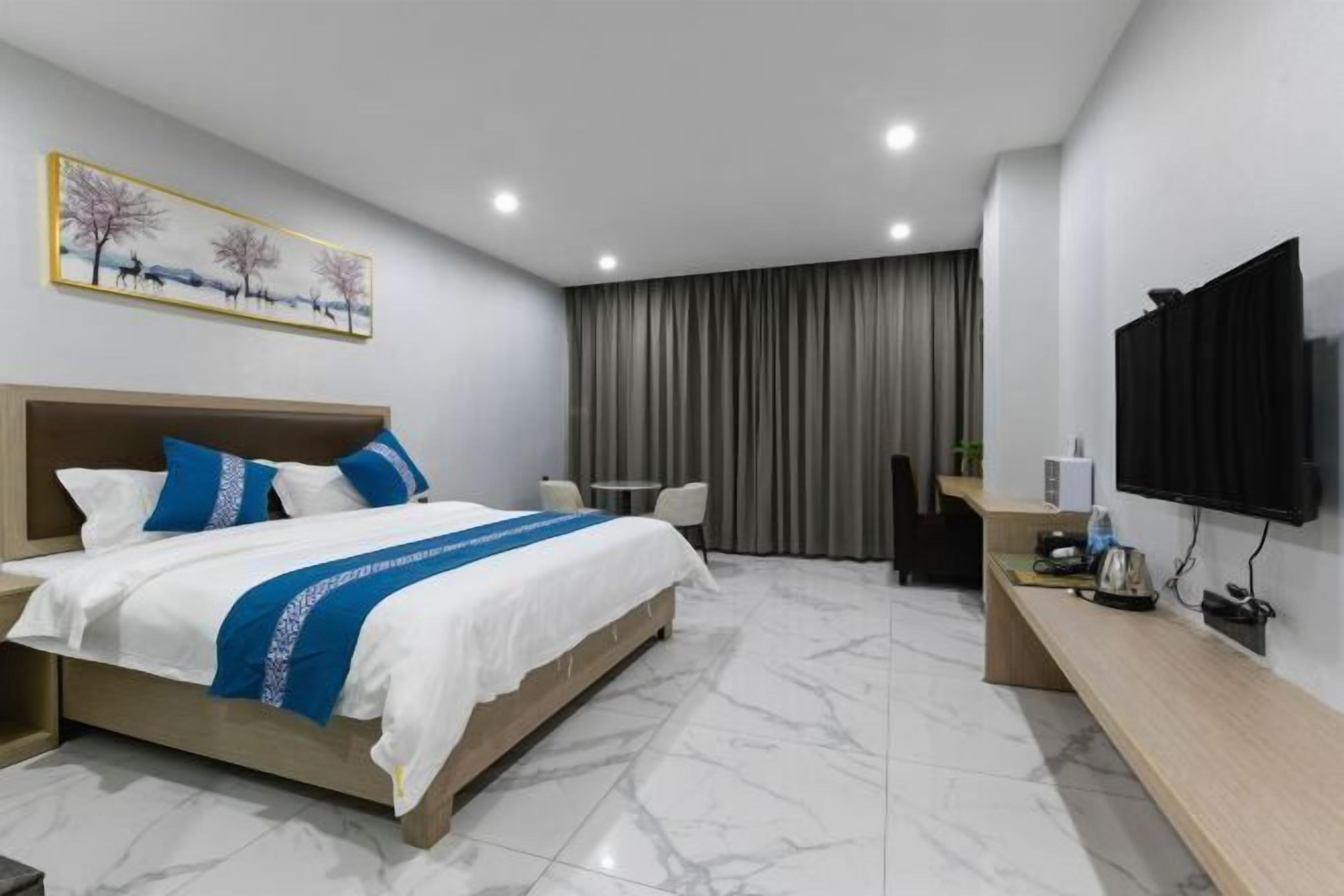 A hotel room with a bed, a desk, a chair, a television, and a painting on the wall.