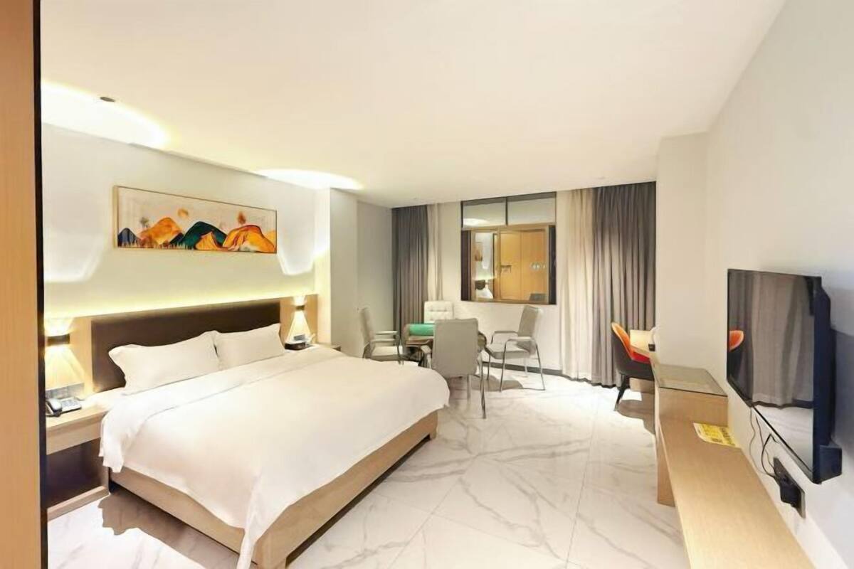 A hotel room with a large bed, a desk with a chair, a television, and a painting on the wall.