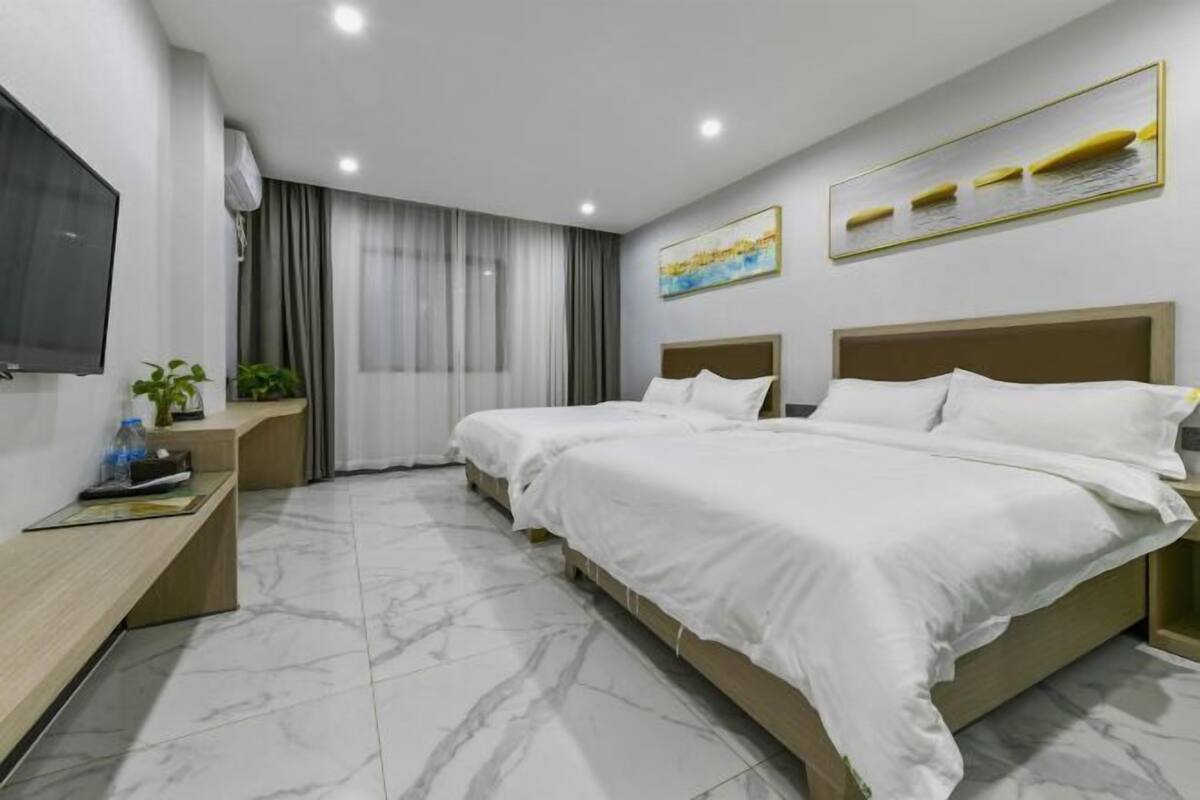 A modern hotel room with two beds, a TV, a desk, and a window with curtains.