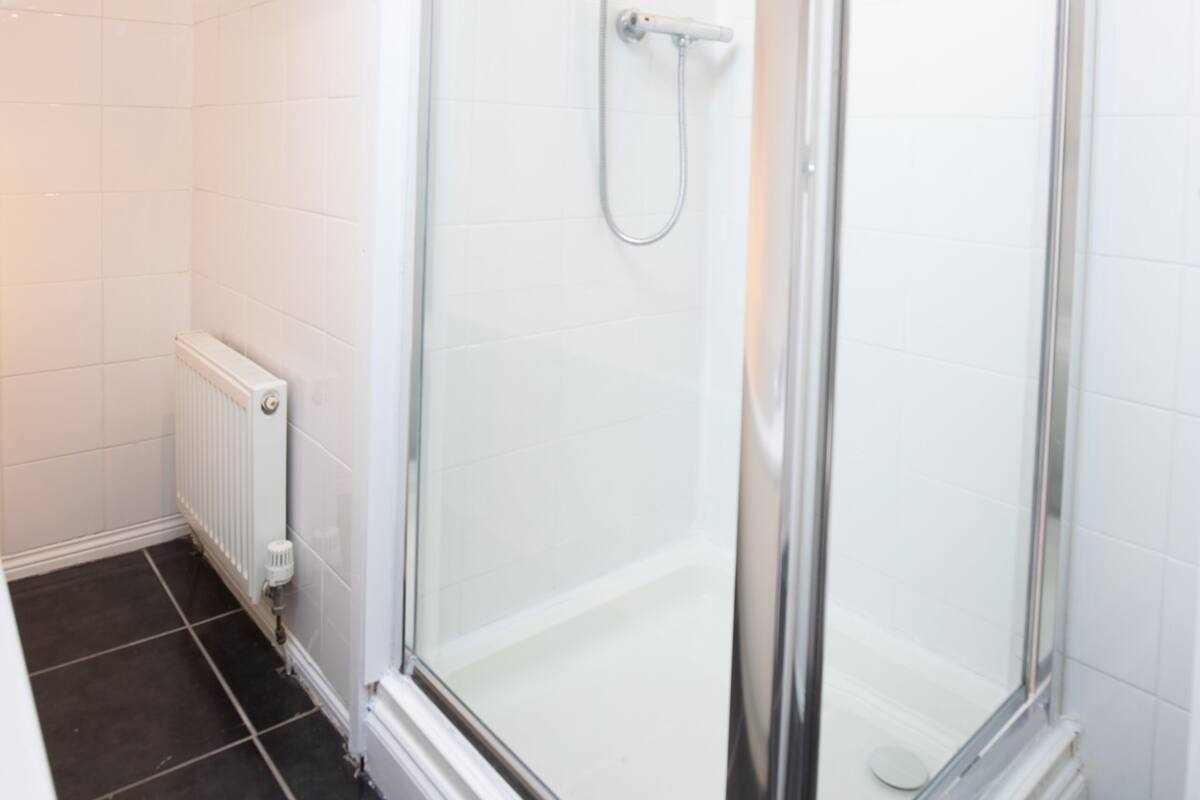 A modern bathroom with a glass-enclosed shower, white tiled walls, and a black tiled floor.