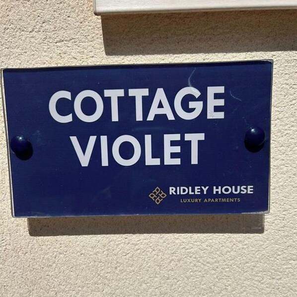 Skilt for 'COTTAGE VIOLET' af RIDLEY HOUSE, der angiver, at det er en luksuslejlighed.