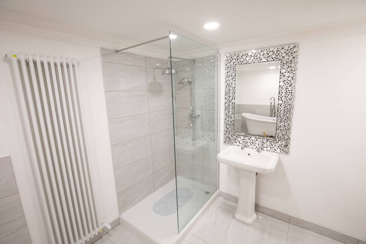 A modern bathroom with a glass-enclosed shower, a pedestal sink, and a decorative mirror.