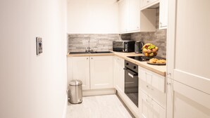 A modern kitchen with white cabinets, a stainless steel sink, a microwave, an oven, and a trash can. - Ridley House Apartments (Yarm)