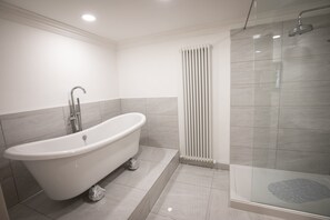 A modern bathroom with a freestanding bathtub, a glass-enclosed shower, and a white radiator. - Ridley House Apartments (Yarm)