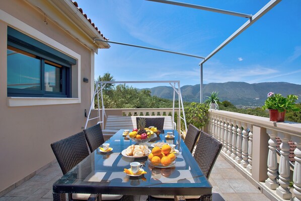 Mesa al aire libre con vistas a montañas, un balcón con barandilla y una planta en maceta.