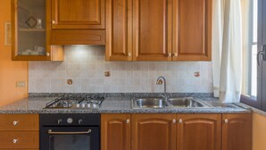 Une cuisine avec des meubles de rangement en bois, une cuisinière à gaz, un évier et une fenêtre avec des rideaux.