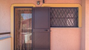 Une porte fermée avec un portail en métal, une fenêtre protégée par une grille en métal et un mur à la texture particulière.