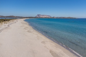 A beach with clear water, a stone wall, and distant mountains. - Vacation Home "Quadrilocale Suaredda" with Balcony (Suaredda-traversa)
