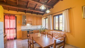 Une cuisine avec des meubles de rangement en bois, une table à manger, des chaises et une fenêtre avec des rideaux.