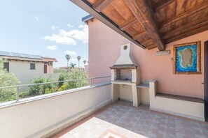 A balcony with a barbecue grill, a stone wall with a painting, and a view of neighboring buildings.