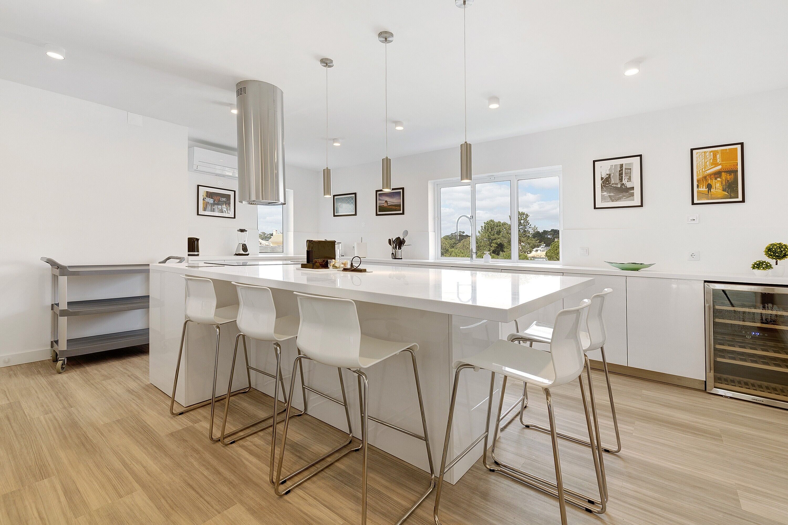 A modern kitchen with a large island, bar stools, stainless steel appliances, and framed pictures on the walls.