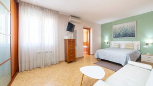 Quarto de hotel com uma cama, uma mesinha, cômoda, televisão e um quadro na parede.