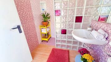 Un bagno con parete piastrellata, un lavandino, uno specchio, un carrello giallo, un tappeto rosso e una pianta in vaso.