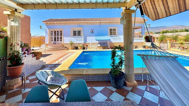 Uma área à beira da piscina com vista para uma casa, uma rede e uma cadeira.