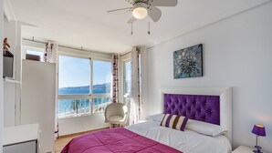 A bedroom with a bed, a ceiling fan, a window with a view, a chair, and a nightstand. - Apartment 'Bonito Apartamento Frente Al Mar' with Sea View, Wi-Fi and Air Conditioning (Salobreña)