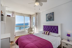 A bedroom with a bed, a ceiling fan, a window with a view, a chair, and a nightstand.